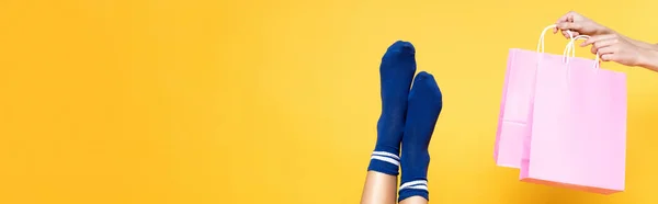 Жіночі ноги в синіх шкарпетках біля рожевих паперових мішків ізольовані на жовтому тлі, банер — стокове фото