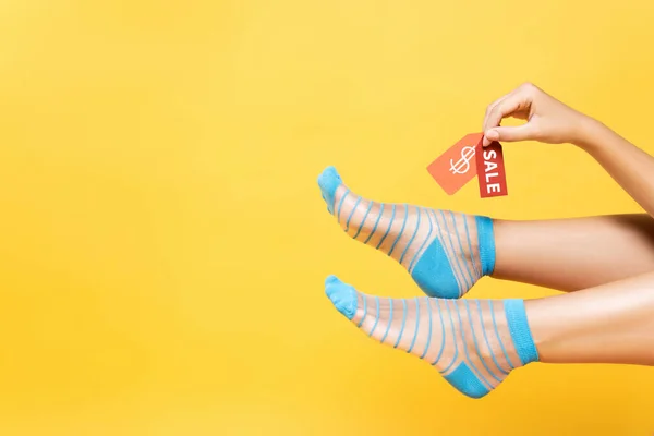 Vista cortada da mulher usando meias listradas, segurando tags com símbolo de dólar e palavra de venda isolada no amarelo — Fotografia de Stock