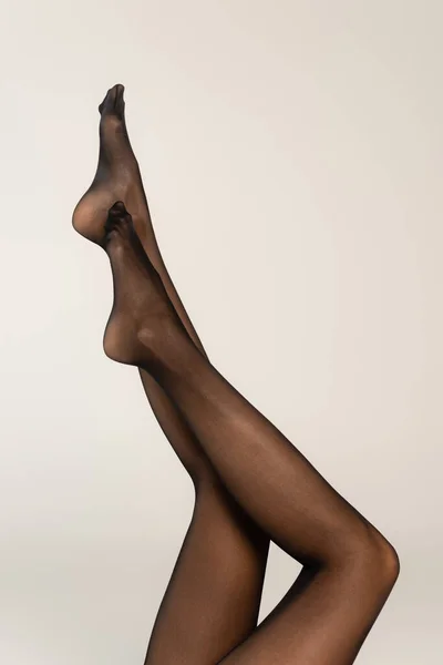 Vista recortada de las piernas femeninas en el aire, con medias negras aisladas en gris - foto de stock
