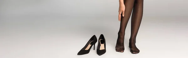Mulher de collants escuros de pé perto de sapatos pretos em fundo cinza, banner — Fotografia de Stock