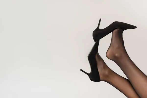 Обрізаний вид жінки з ногами в повітрі, в чорних колготках і взутті з підборами ізольовані на сірому — стокове фото