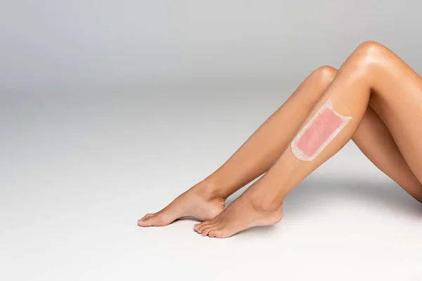 Cropped view of woman smooth legs with pink wax stripe on grey — Stock Photo