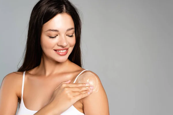 Ritratto di giovane donna sorridente che applica crema sulla spalla isolata su grigio — Foto stock