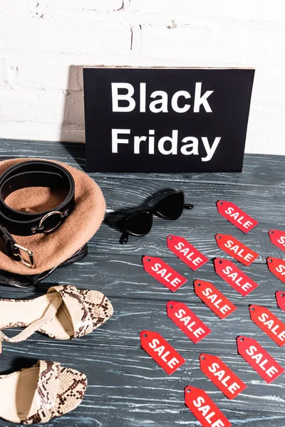 Scarpe, occhiali da sole, berretto e cintura vicino bordo con venerdì nero e targhette con scritte in vendita in superficie — Foto stock