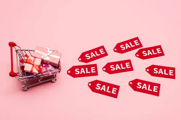 Top view of toy shopping cart with presents near tags with sale lettering on pink, black friday concept — Stock Photo