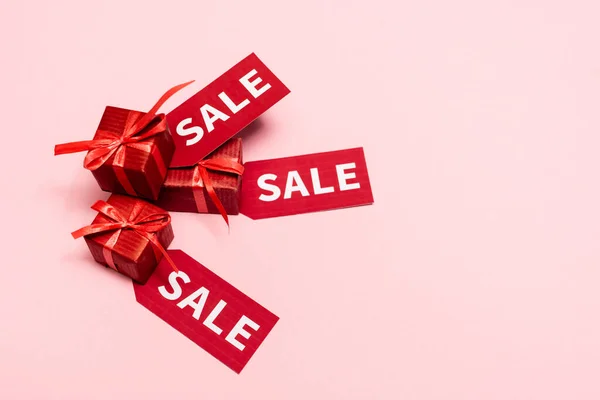 Top view of red labels with sale lettering near presents on pink — Stock Photo