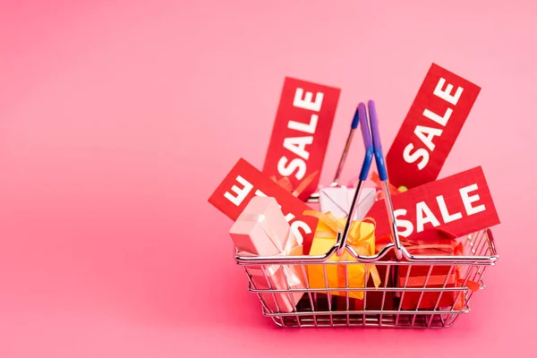 Shopping basket with presents and red sale tags on pink — Stock Photo