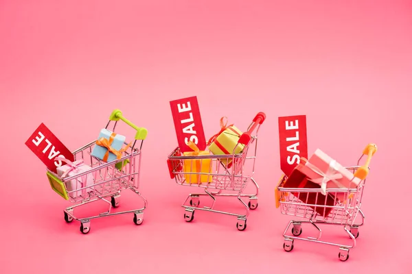 Colorful presents in shopping carts with sale tags on pink, black friday concept — Stock Photo