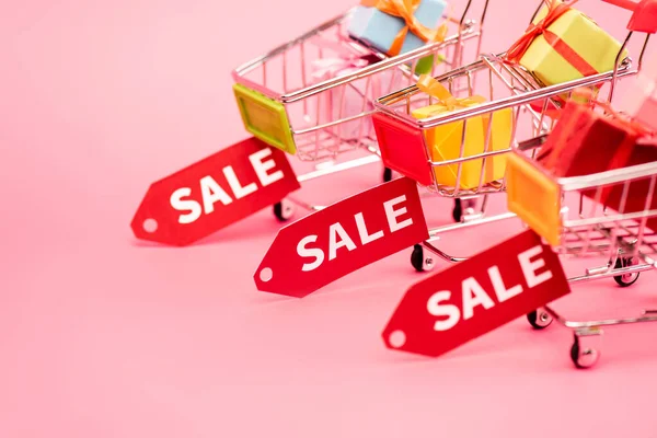 Selective focus of colorful presents in shopping carts with sale tags on pink, black friday concept — Stock Photo