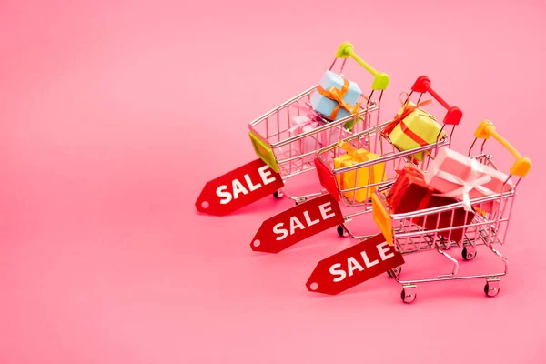 Colorful gifts in shopping carts with sale tags on pink, black friday concept — Stock Photo