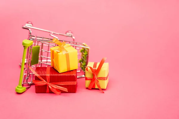 Colorful presents near shopping trolley on pink, black friday concept — Stock Photo