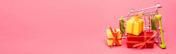 Horizontal crop of colorful presents near shopping trolley on pink, black friday concept — Stock Photo