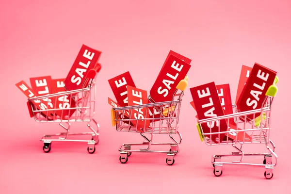 Étiquettes rouges avec lettrage de vente dans des chariots d'achat sur rose — Photo de stock