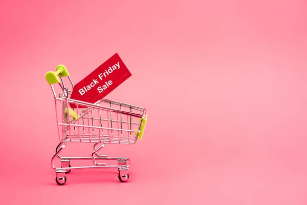 Etiqueta roja con letras de venta de viernes negro en el carrito de la compra en rosa - foto de stock