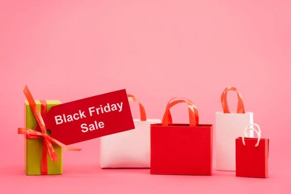 Geschenkbox mit Black Friday Sale Tag in der Nähe von Einkaufstaschen auf rosa — Stockfoto