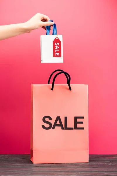 Cropped view of woman holding small shopping bag with sale tag near paper package on pink, black friday concept — Stock Photo