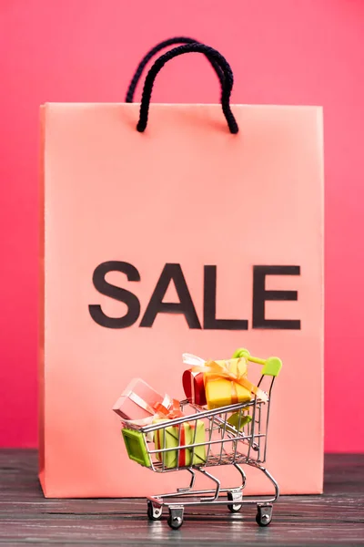 Selective focus of toy trolley with gifts near paper bag with sale lettering on pink, black friday concept — Stock Photo