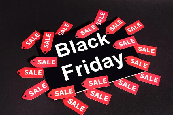 Placard with black friday lettering near sale tags on dark background — Stock Photo