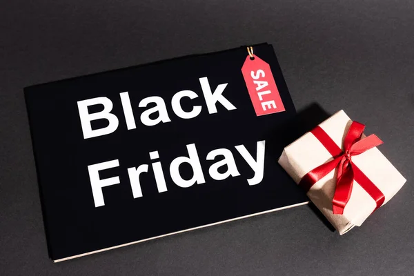 Vue du dessus de la boîte cadeau avec ruban et étiquette de vente près de placard noir vendredi sur fond sombre — Photo de stock