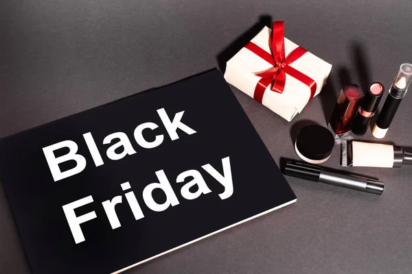 Hochwinkelansicht eines Plakats mit schwarzem Freitag-Schriftzug und Geschenk in der Nähe von dekorativer Kosmetik auf dunklem Hintergrund — Stockfoto