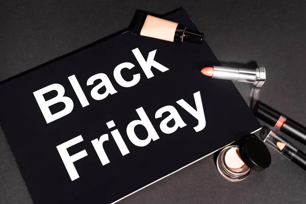 Hochwinkelansicht eines Plakats mit schwarzem Freitag-Schriftzug in der Nähe von dekorativer Kosmetik auf dunklem Hintergrund — Stockfoto