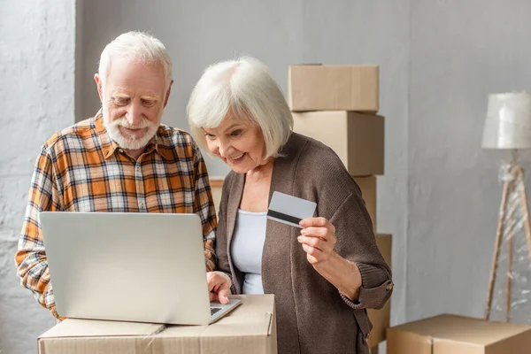 Sonriente pareja de ancianos haciendo la compra en línea utilizando el ordenador portátil y tarjeta de crédito - foto de stock