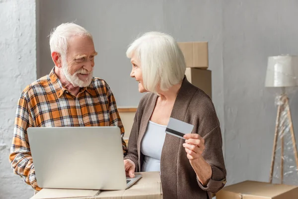 Sorrindo casal sênior fazendo compra on-line usando laptop e cartão de crédito — Fotografia de Stock
