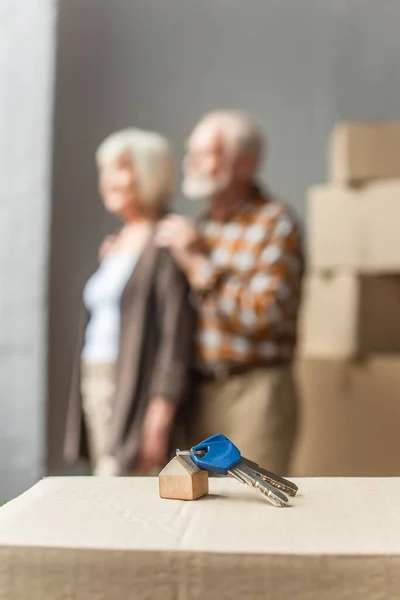 Vue floue du couple de personnes âgées emménageant dans une nouvelle maison et des clés au premier plan, concept mobile — Photo de stock