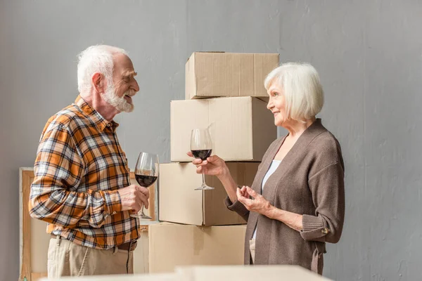 Счастливая пожилая пара празднует переезд в новый дом с бокалами вина — стоковое фото