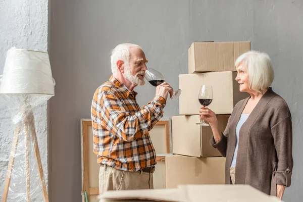 Heureux couple de personnes âgées célébrant déménagement dans une nouvelle maison avec des verres de vin — Photo de stock