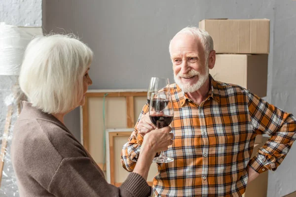 Smiling senior couple clinking glasses of wine, moving concept — Stock Photo