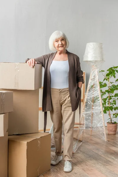 Ganzkörperansicht einer Seniorin, die sich auf Kisten lehnt, bewegtes Konzept — Stockfoto