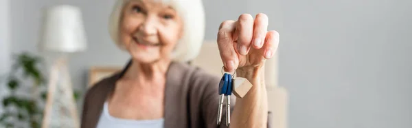 Panoramic shot of blurred smiling senior woman holding keys, moving concept — Stock Photo