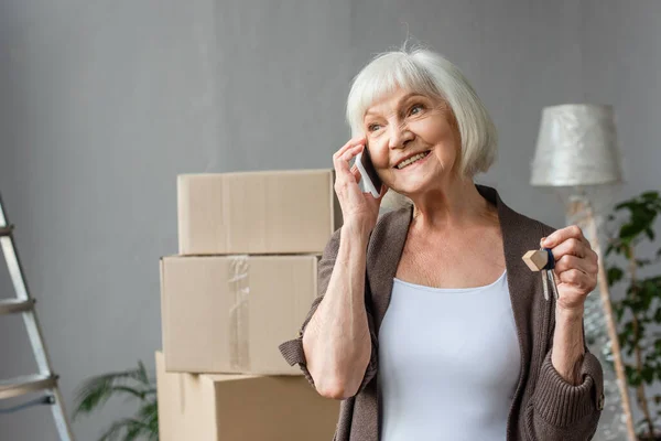 Happy senior woman talking on phone and holding keys in new house, moving concept — Stock Photo