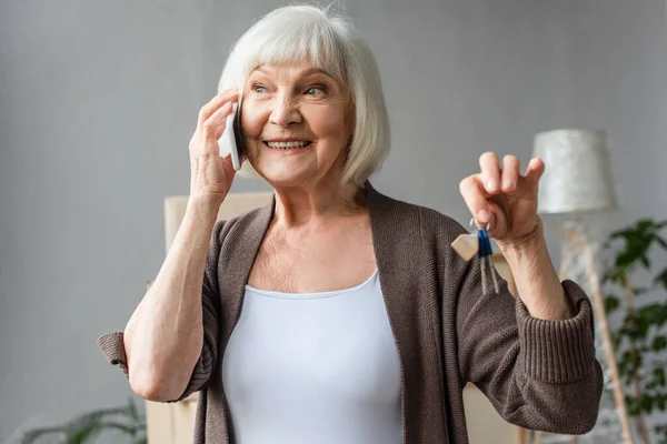 Feliz mujer mayor hablando por teléfono y sosteniendo las llaves en la nueva casa, concepto en movimiento — Stock Photo