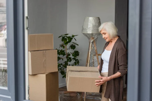 Cheerful senior woman holding cardboard box, moving concept — Stock Photo