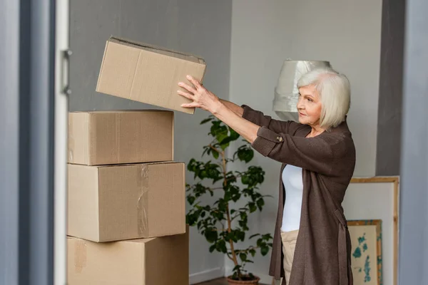 Cheerful senior woman arranging cardboard boxes, moving concept — Stock Photo