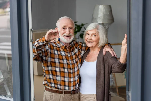 Laughing senior man holding keys and embracing wife in new house — Stock Photo