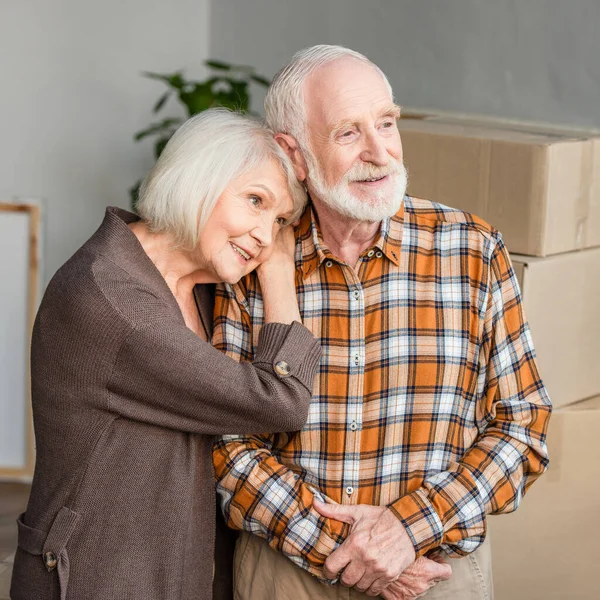 Cheerful senior woman leaning on husband shoulder in new house — Stock Photo