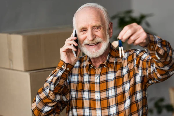 Счастливый пожилой человек, разговаривающий по телефону и держащий ключи от нового дома, движущаяся концепция — стоковое фото