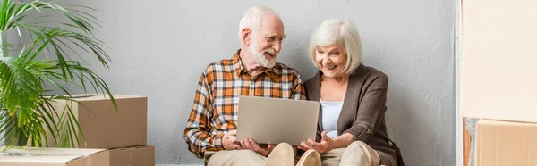 Plan panoramique de couple de personnes âgées en utilisant ordinateur portable assis sur le sol — Photo de stock