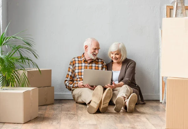 Feliz pareja de ancianos utilizando el ordenador portátil sentado en el suelo, concepto en movimiento - foto de stock