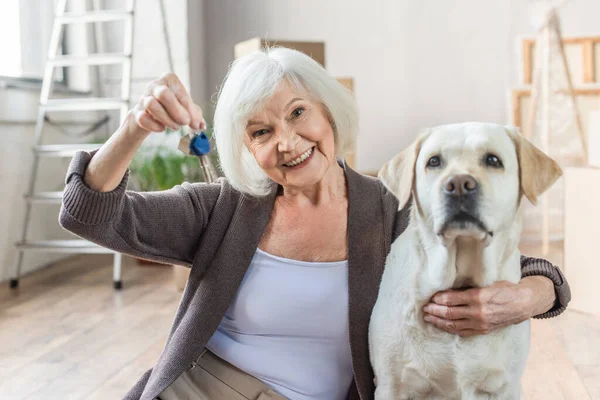Femme âgée souriante embrassant chien et tenant les clés, concept mobile — Photo de stock