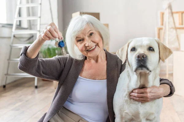 Sorridente mulher sênior abraçando cão e segurando chaves, conceito em movimento — Fotografia de Stock