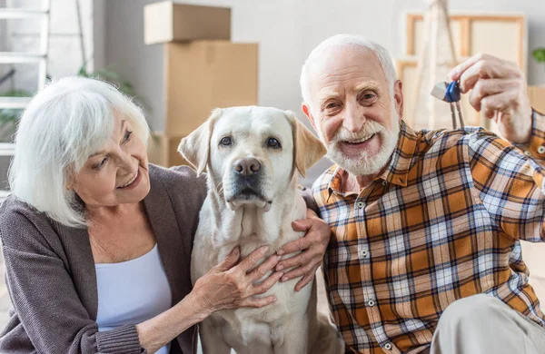 Senior woman embracing dog while husband holding keys, moving concept — Stock Photo