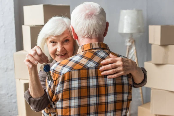 Donna anziana sorridente che tiene le chiavi e abbraccia il marito, concetto commovente — Foto stock