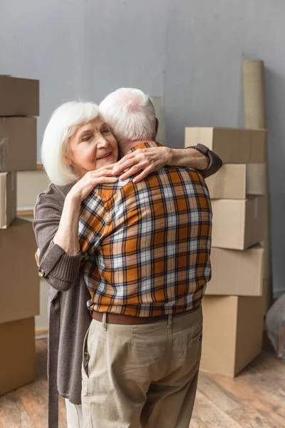 Senior woman with closed eyes hugging husband in new house, moving concept — Stock Photo