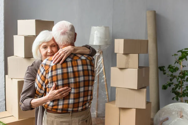 Senior woman with closed eyes hugging husband in new house, moving concept — Stock Photo