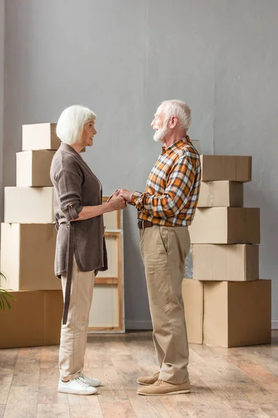 Full length view of senior couple holding hands and looking at each other in new house, moving concept — Stock Photo