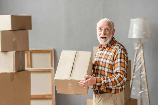 Surpris homme âgé tenant boîte en carton dans une nouvelle maison, concept mobile — Photo de stock